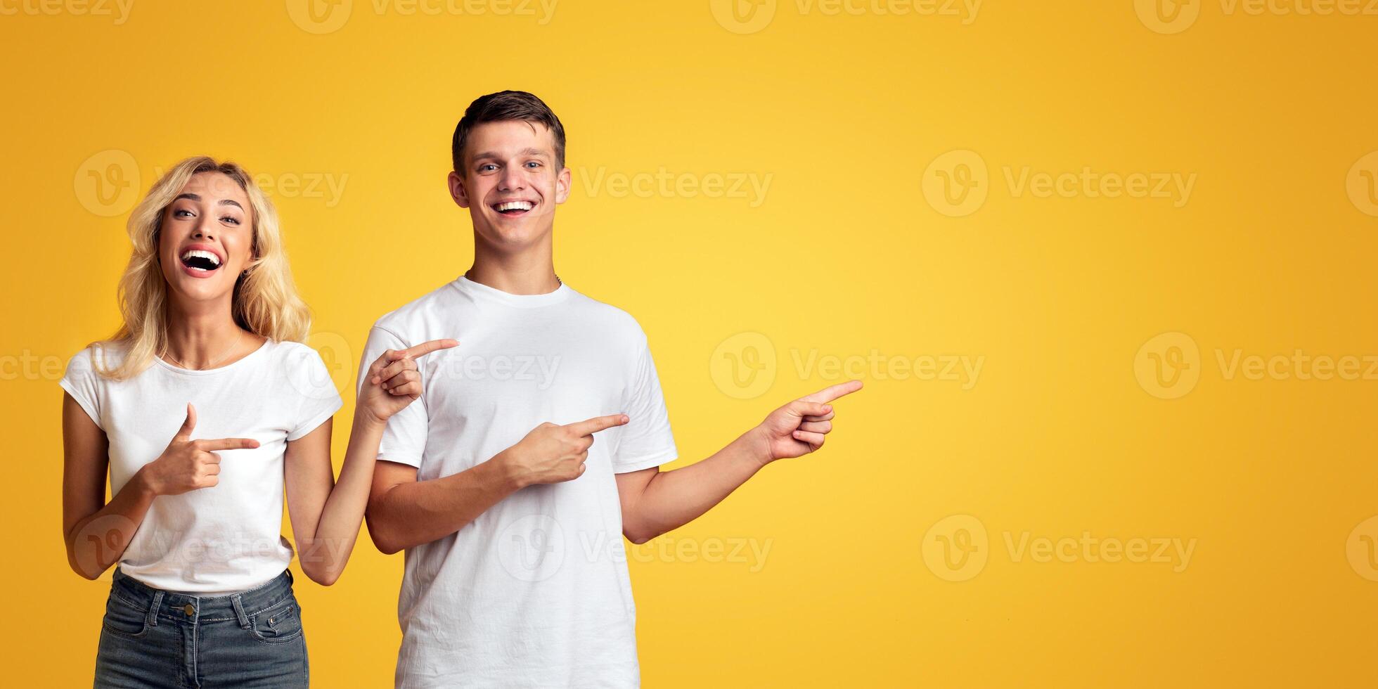 Joyful young guy and girl pointing away at copy space on yellow background photo