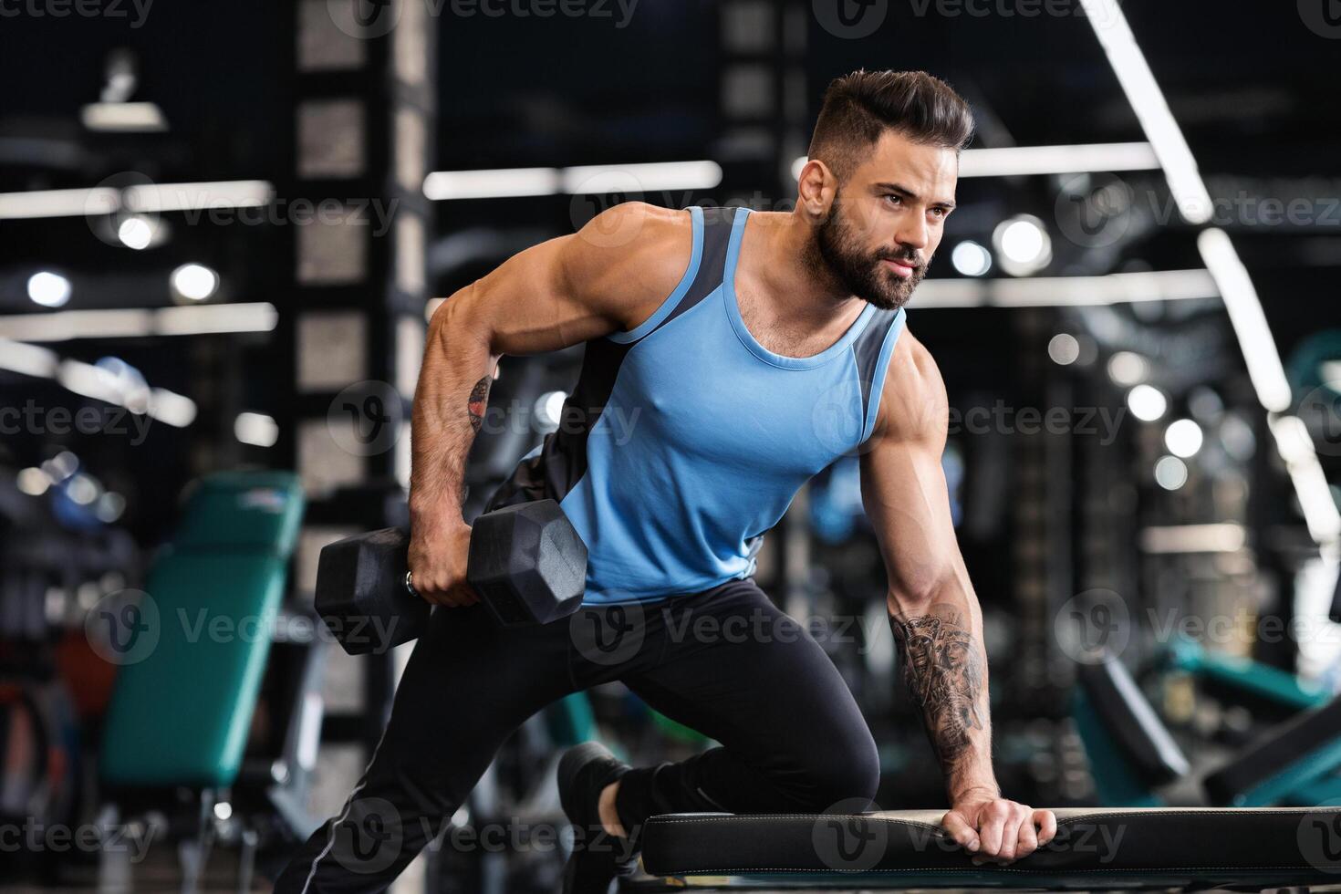 Millennial muscular man working out in gym, doing exercises with dumbbells at biceps, free space photo