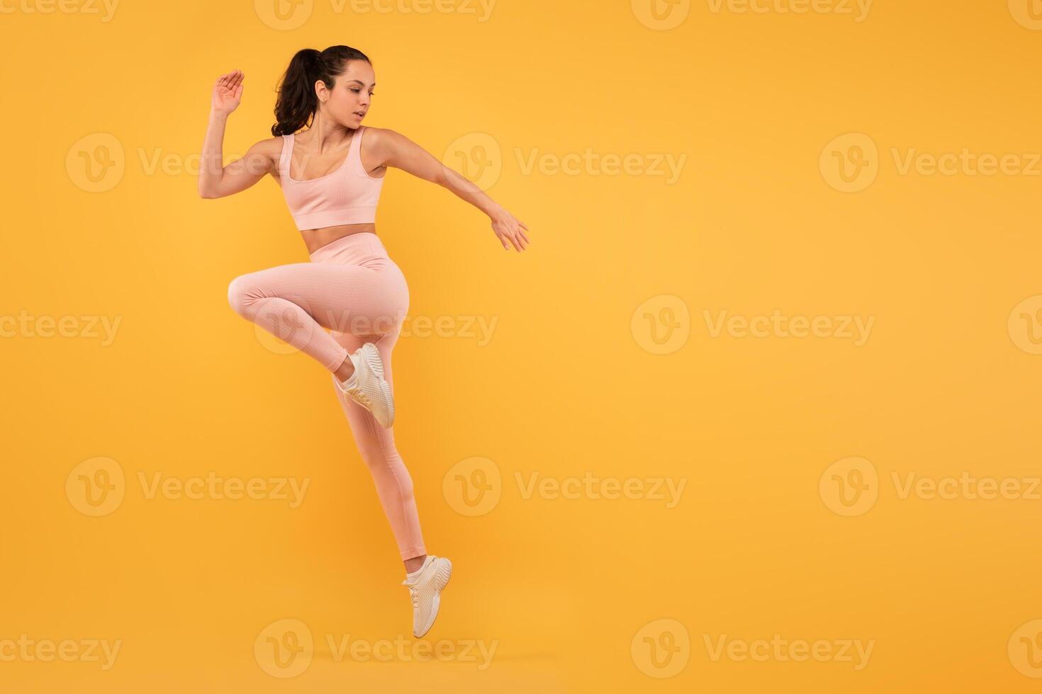 A woman wearing a pink outfit is captured mid-air as she jumps. Her joyful expression is evident as she defies gravity. The background is blurred, emphasizing her movement, copy space photo