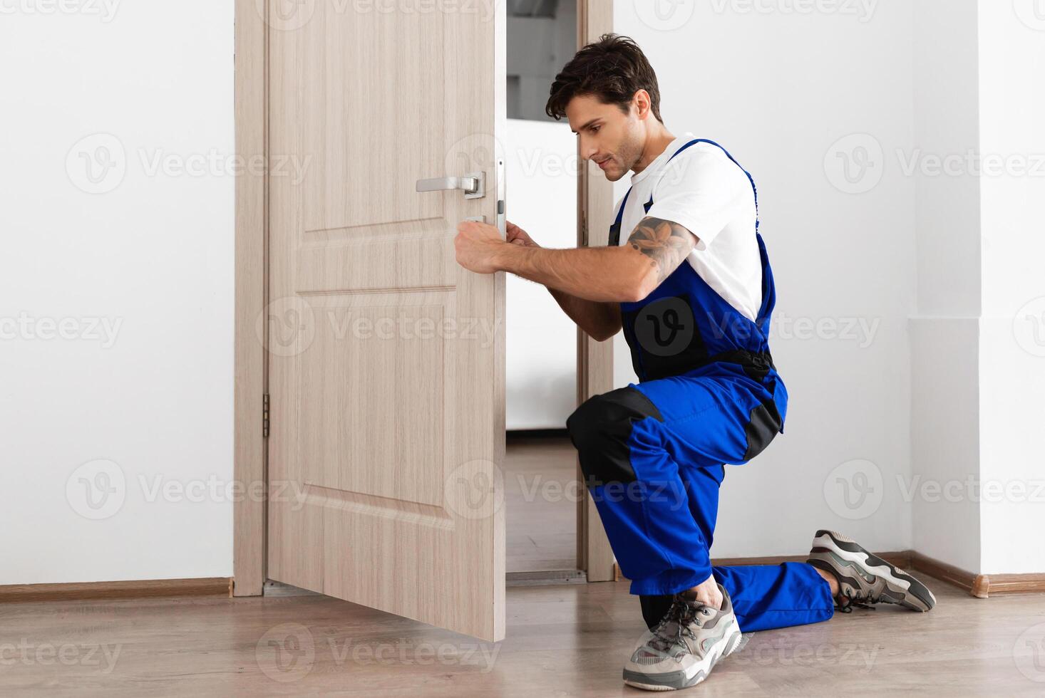 instalación de un bloquear en el frente de madera Entrada puerta. retrato de joven cerrajero obrero en azul uniforme instalando puerta mando. profesional reparar servicio. mantenimiento concepto foto