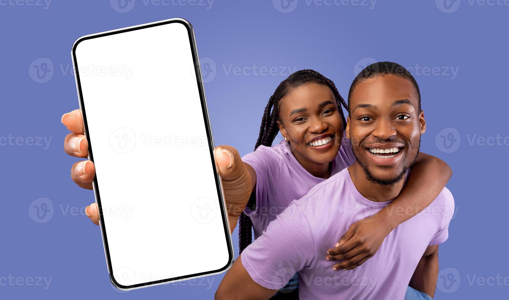 A happy black couple poses for a picture while holding up a smartphone with a blank screen. They are both smiling and looking at the camera. photo