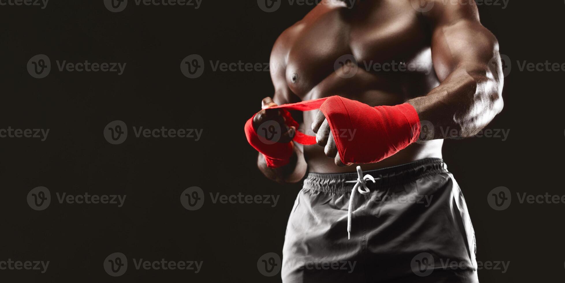 Strong african man wrapping hands with boxing wraps, close up on black background photo