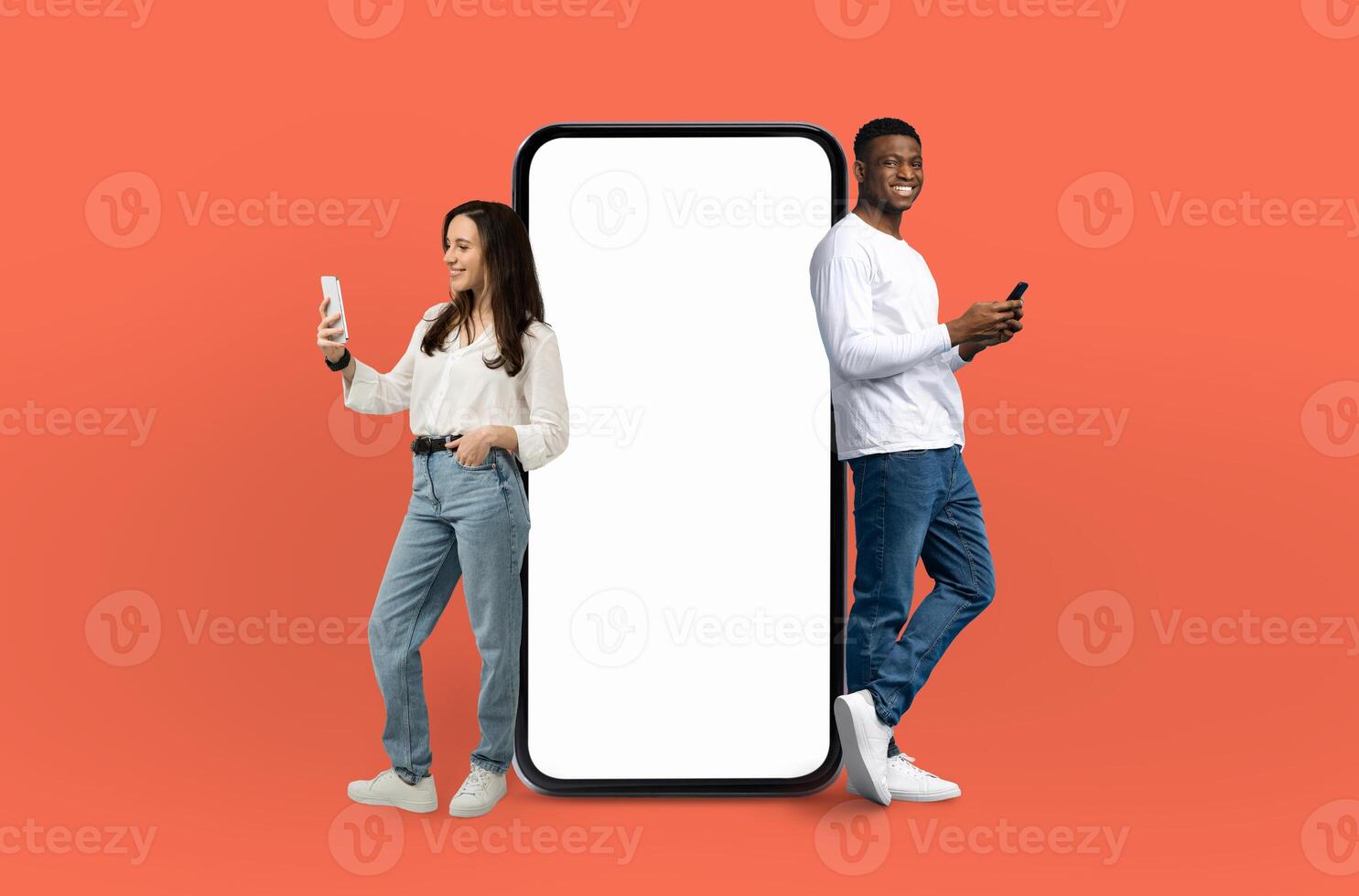 A man and woman are positioned next to a blank screen against an orange background. They are standing upright and appear to be focusing on the empty screen in front of them. photo