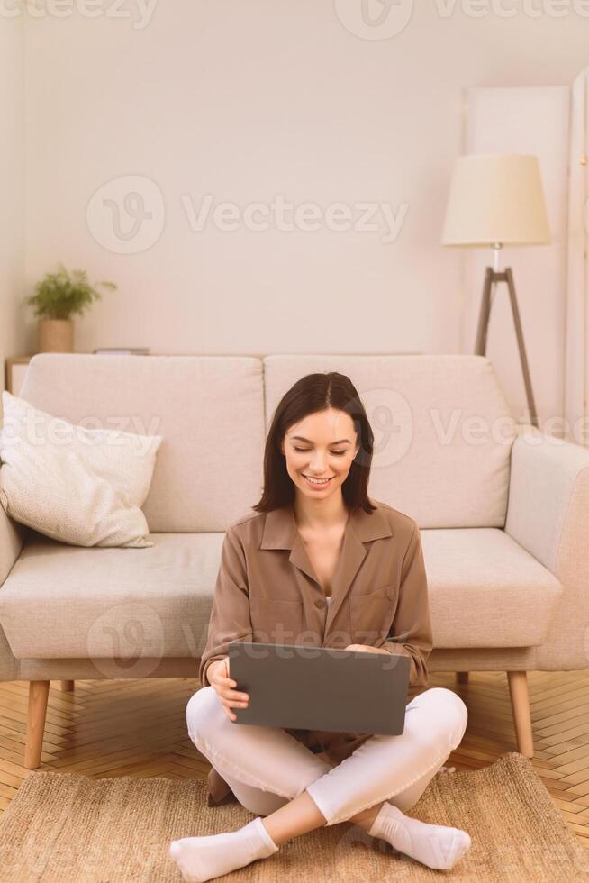 Surfing Internet. Happy smiling woman working on laptop computer, sitting on the floor with legs crossed, copyspace photo