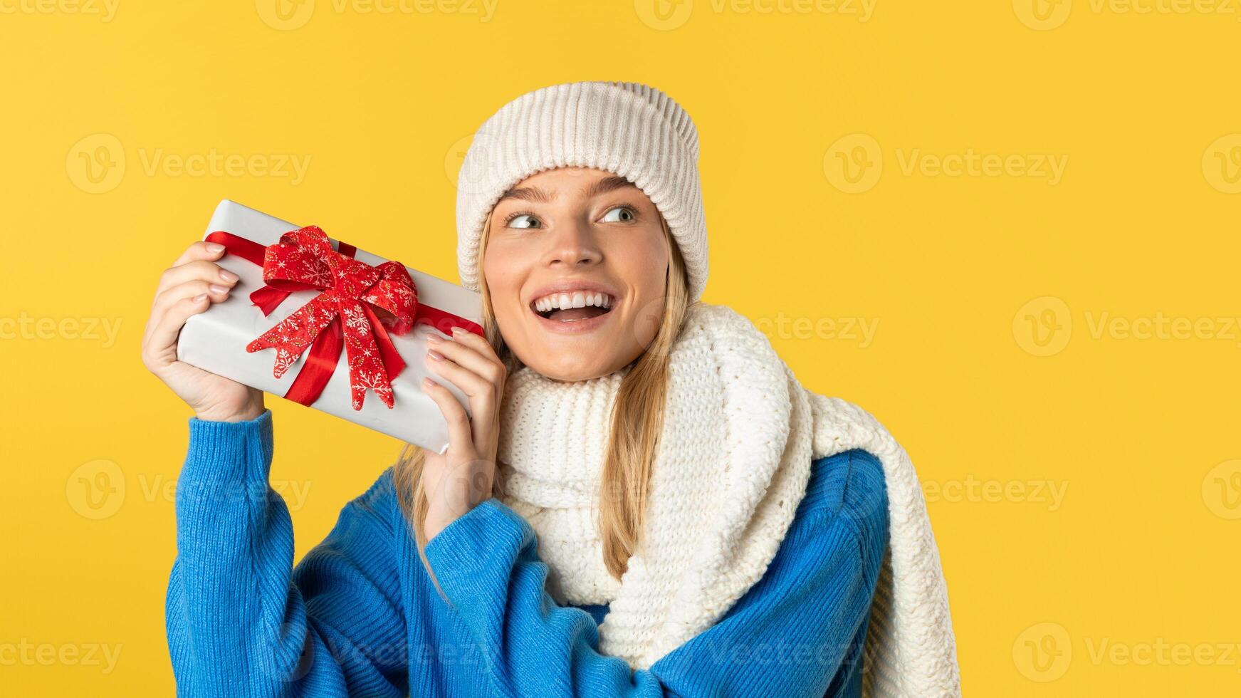 A woman wearing a blue sweater is holding a wrapped present in her hands. She appears to be standing, with a neutral expression on her face. photo
