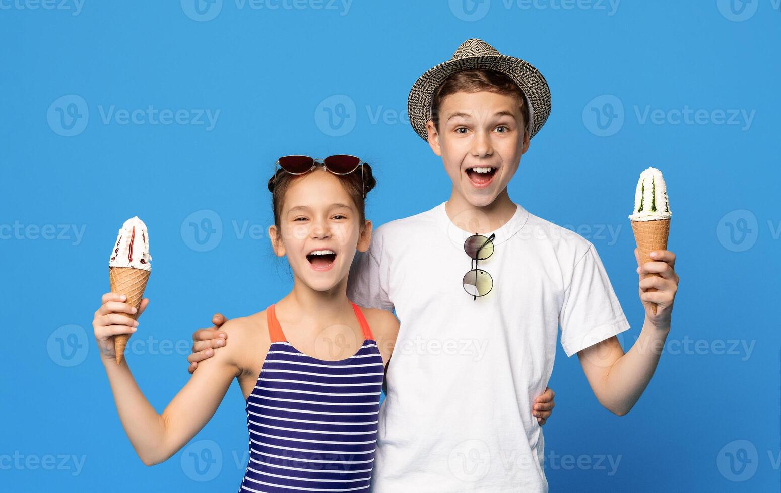 Happy little boy and girl embracing with ice cream cones, blue studio background photo