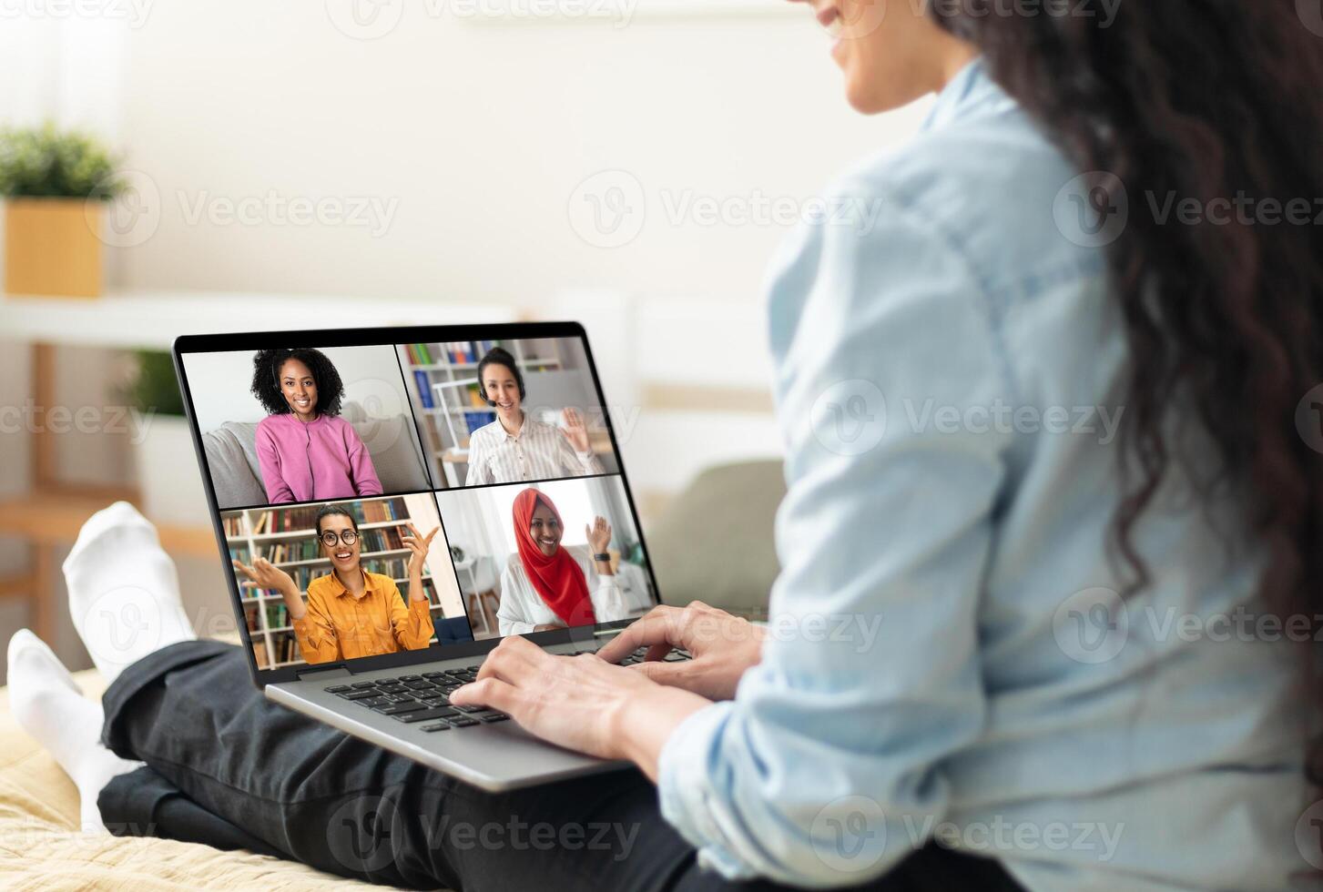 A woman is sitting on a couch, using a laptop to participate in a virtual meeting. Her feet are up on the couch, and she is engaged in the conversation with her colleagues. photo