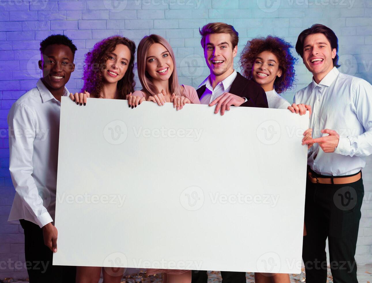 Group Of Multiethnic Young People Holding Blank White Poster Smiling At Camera Standing Over Wall Indoor. Mockup photo