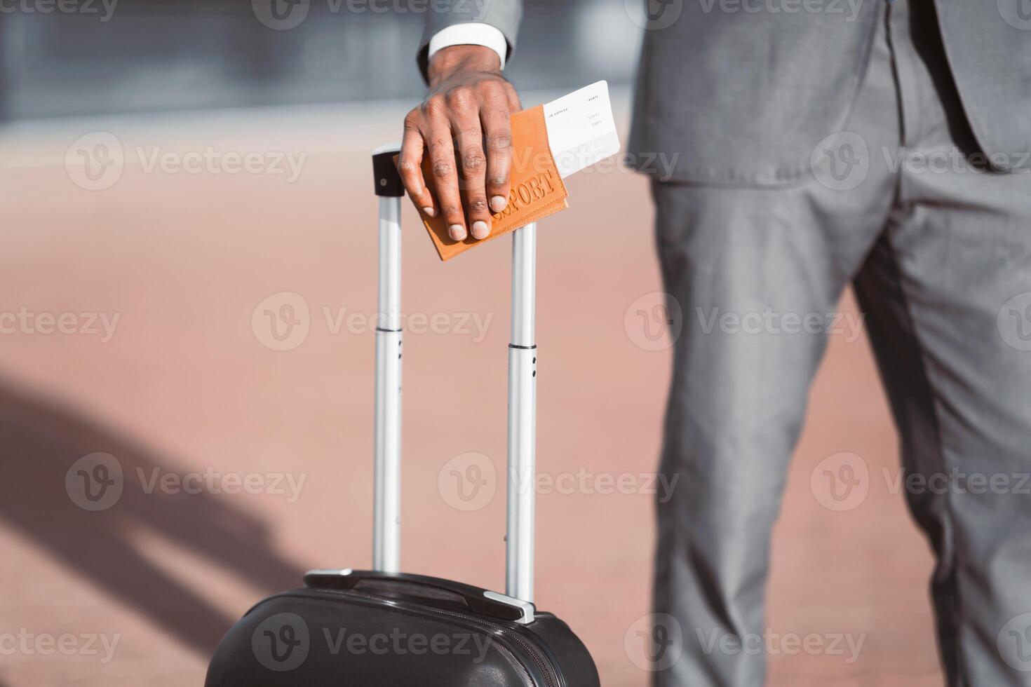 Cropped of black businessman with passport and flight tickets holding his hand on suitcase, posing outside airport photo