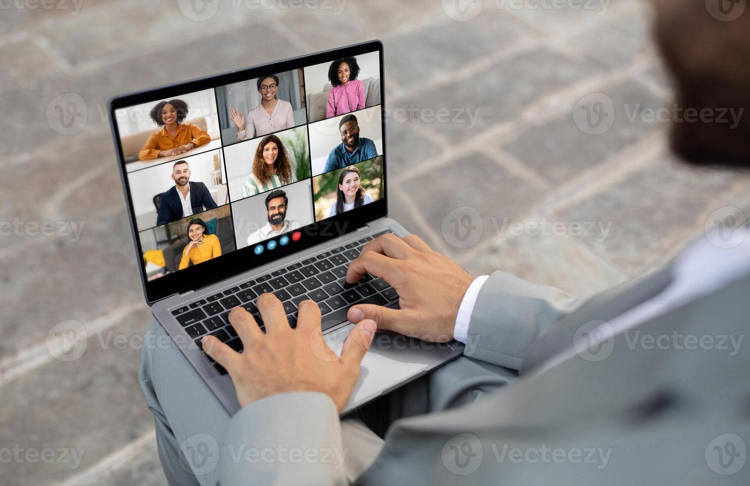 African American business professional is sitting outdoors, engaged in a virtual meeting with multiple colleagues displayed on a laptop screen. The person is typing on the keyboard photo