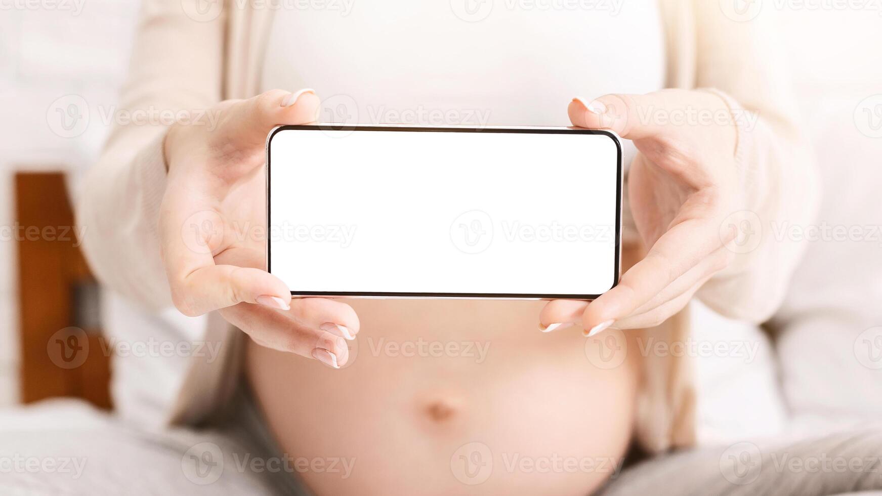 Pregnancy calendar application. Pregnant woman holding cellphone with blank screen near her big belly, mockup, empty space photo