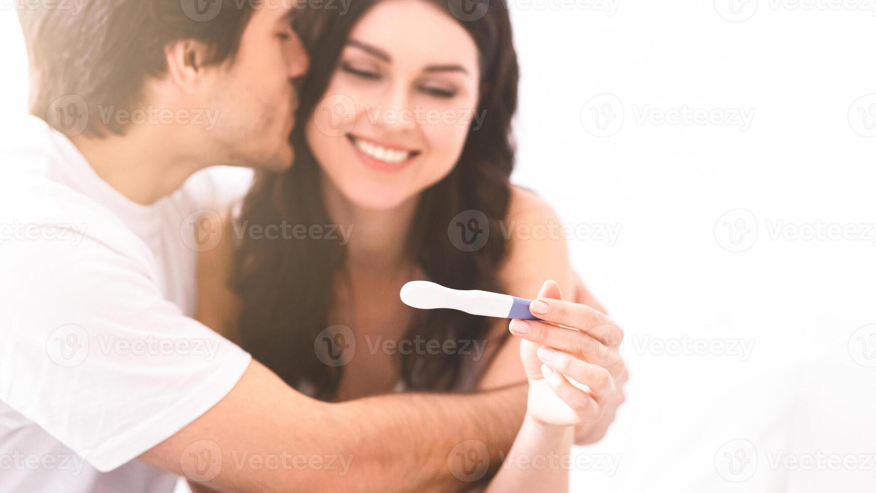 A young couple embraces with excitement as they share the good news of a positive pregnancy test. The woman holds the test up with a big smile, while the man leans in to kiss her on the cheek. photo