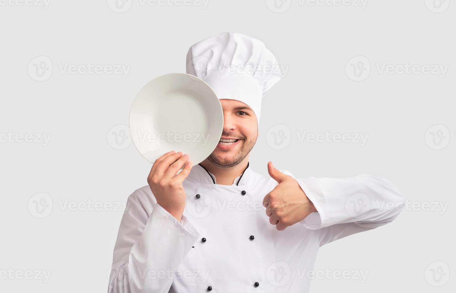 I Like Cooking. Positive Chef Man Gesturing Thumbs-Up Holding Plate Near Face Covering Eye Standing Over White Studio Background. Panorama photo