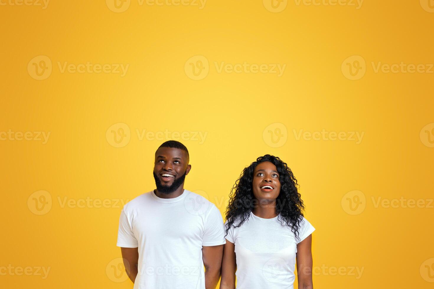 Delighted Black Couple Is Looking Upwards At Free Space, yellow studio background photo