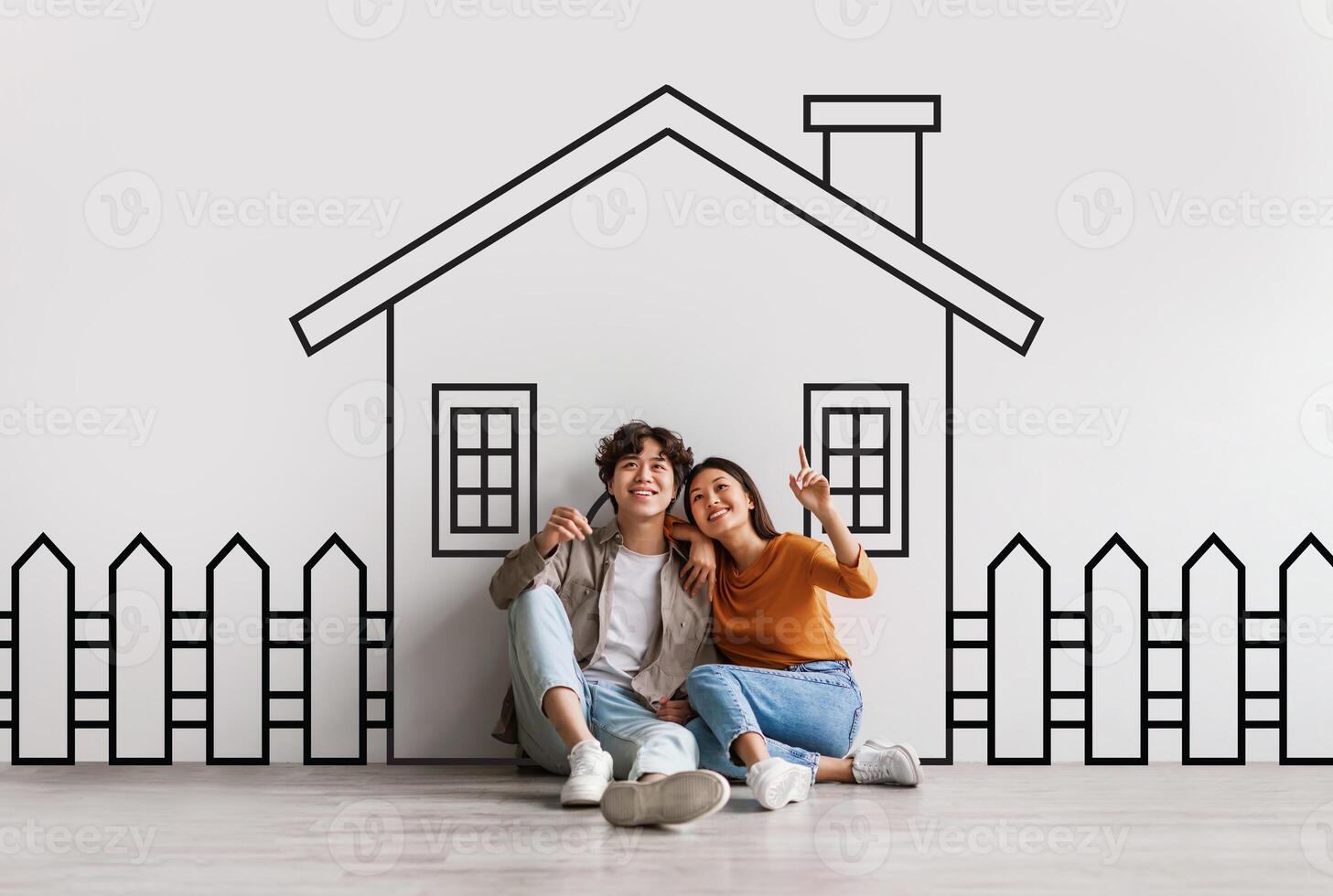 Asian lovers are seated on the ground, facing a detailed drawing of a residential building. The drawing appears to be of a house with multiple windows, a door, and a sloping roof. photo