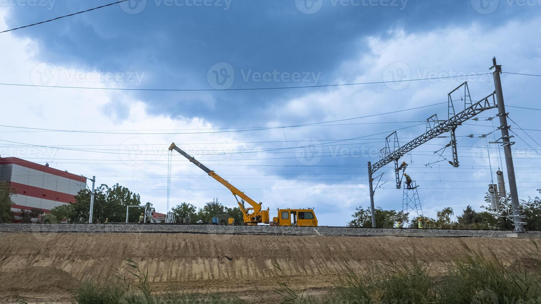 Construction site with heavy machinery and workers installing railway powerlines under a cloudy sky, illustrating infrastructure development photo