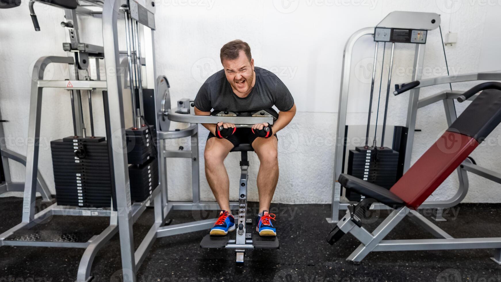 A Caucasian man intensely working out on a back extension machine in a gym, emphasizing fitness goals and challenges photo