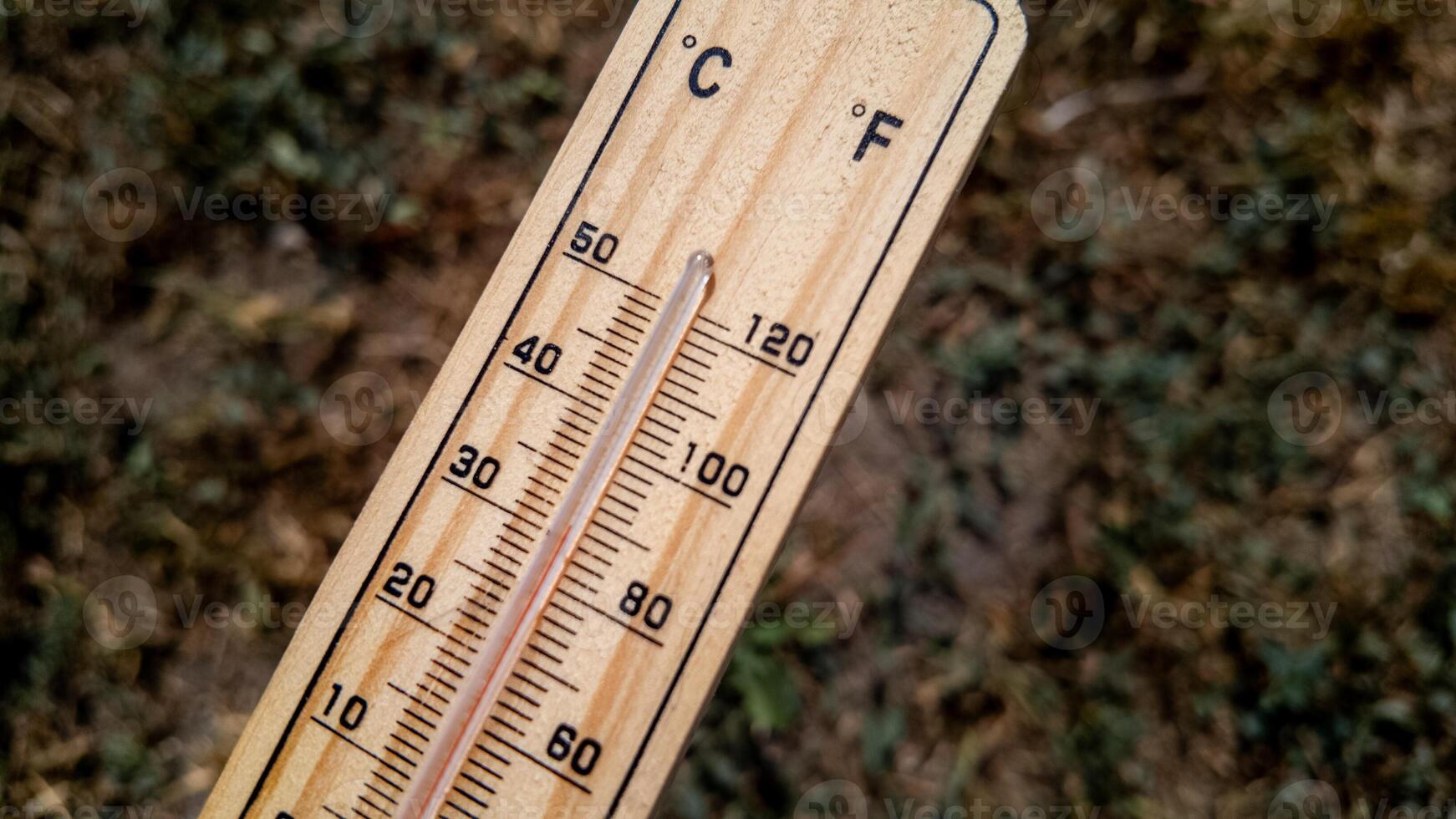 Close up of a wooden thermometer on dry grass indicating extreme heat, relating to summer and climate change awareness photo