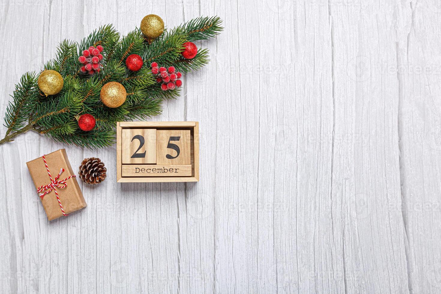 christmas tree branch with toys and gifts and wooden calendar december 25 on wooden background photo