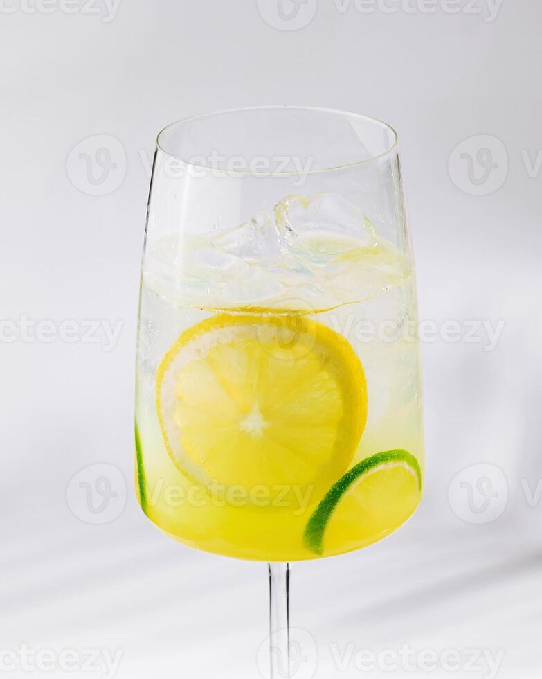 Glass of refreshing lemonade with lemon and lime slices on white background photo