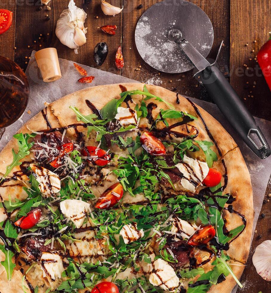 Freshly baked pizza lying on table with ingredients spread around photo