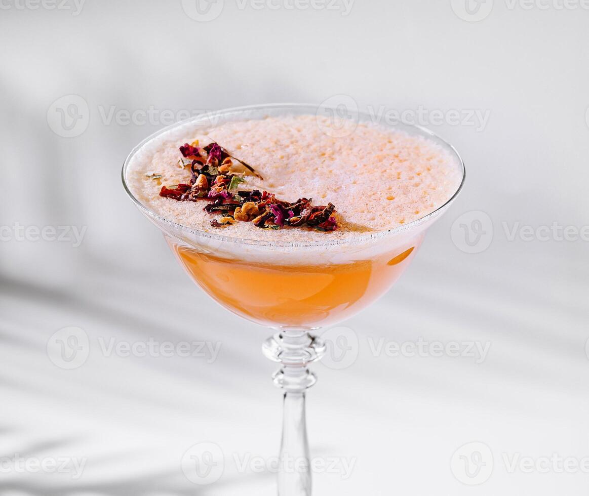 Orange cocktail with edible flowers is standing on a white table photo