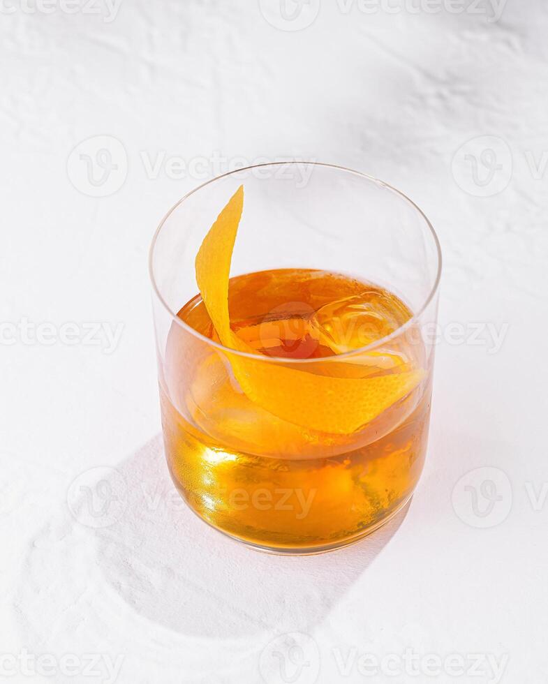 Glass with ice and orange peel is casting a shadow on white table photo