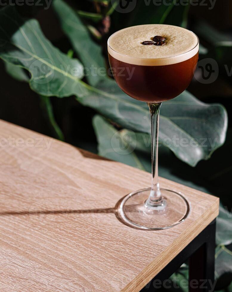 Espresso martini cocktail standing on wooden table in tropical atmosphere photo