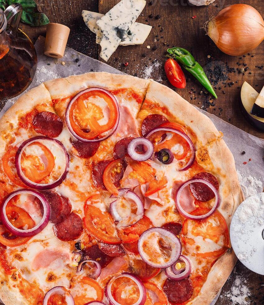 Delicious pizza lying on wooden table with ingredients spread around photo