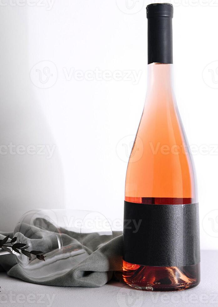 Elegant bottle of rose wine with blank label and empty wineglass laying on tablecloth photo