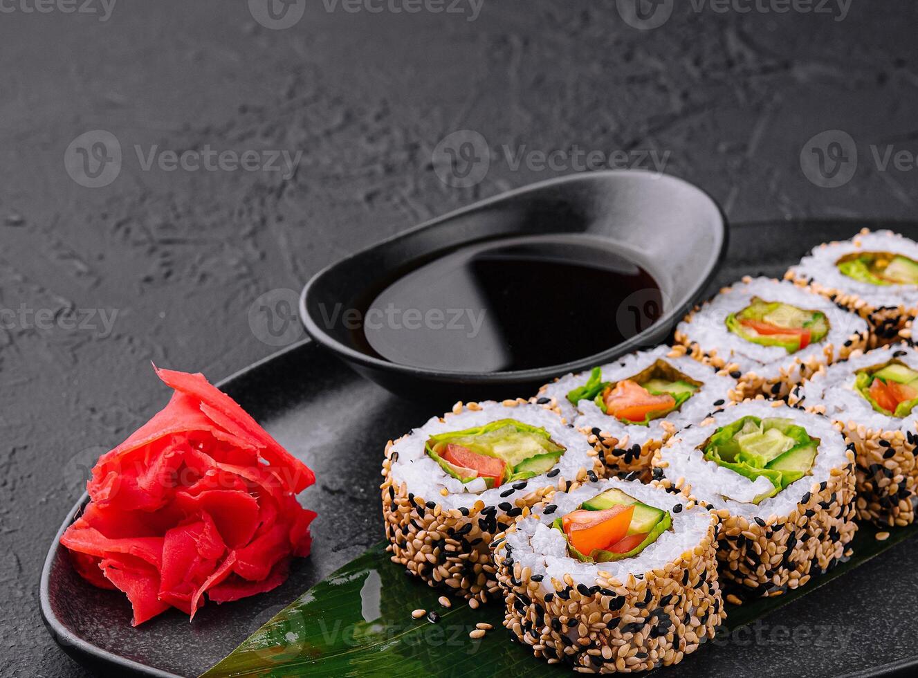 Sushi rolls covered with sesame seeds being served on black stone plate photo