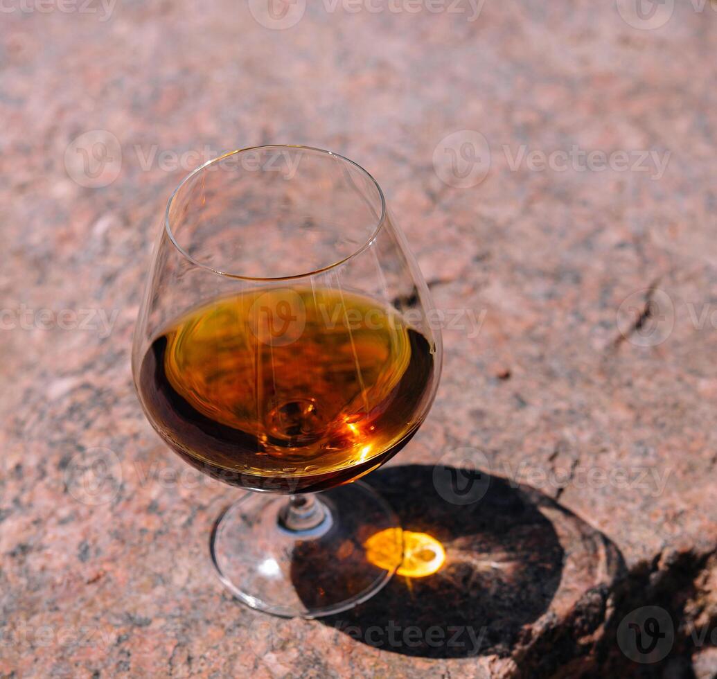 Glass of cognac standing on a rock in the sunlight photo