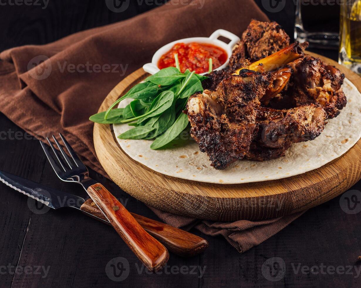 Grilled lamb ribs served on tortilla with spinach and sauce on wooden board photo