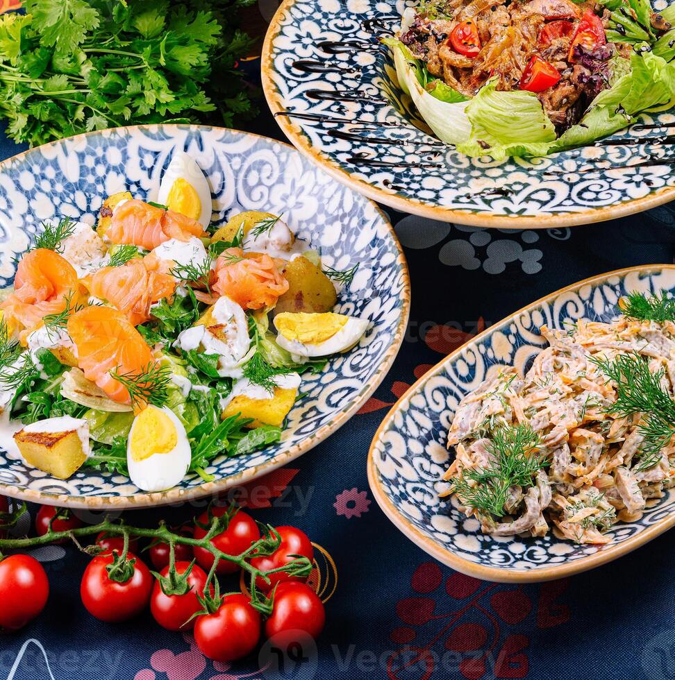 Three plates with different salads are served on a table with a blue tablecloth photo