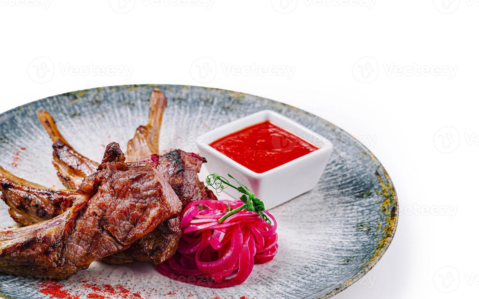 Grilled lamb ribs served on plate with red sauce and onions photo