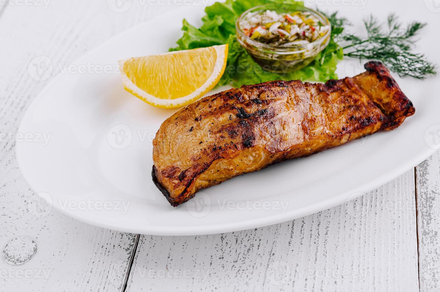 Grilled salmon fillet served on a white plate with lemon and sauce photo