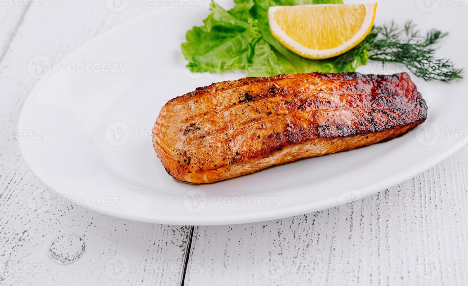 Grilled salmon steak lying on white plate with lemon and lettuce photo