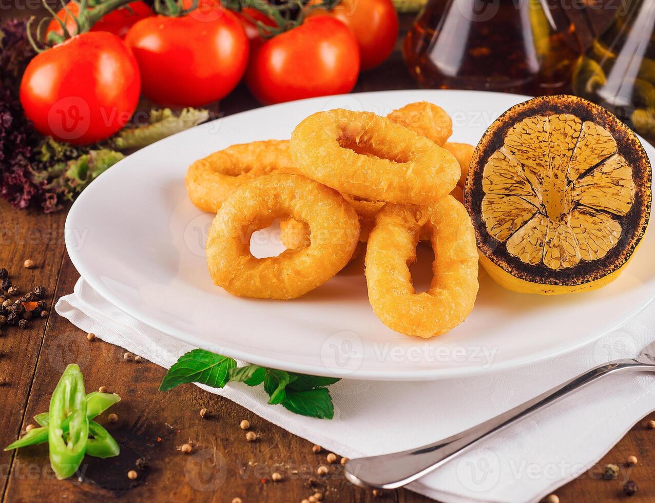 Delicious fried calamari rings served on white plate with grilled lemon and vegetables photo