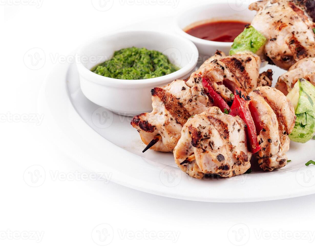 Grilled chicken skewers with vegetables and dipping sauces on white plate photo