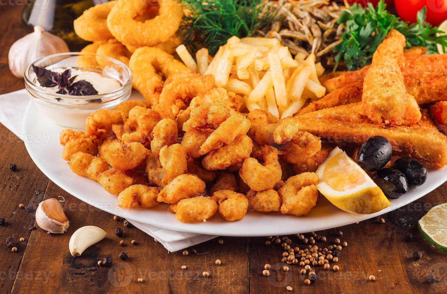 Large plate of delicious breaded seafood with french fries being served on wooden table photo