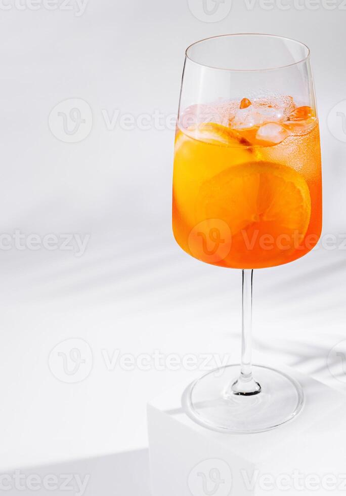 Aperol spritz cocktail standing on white cube casting shadow on white background photo