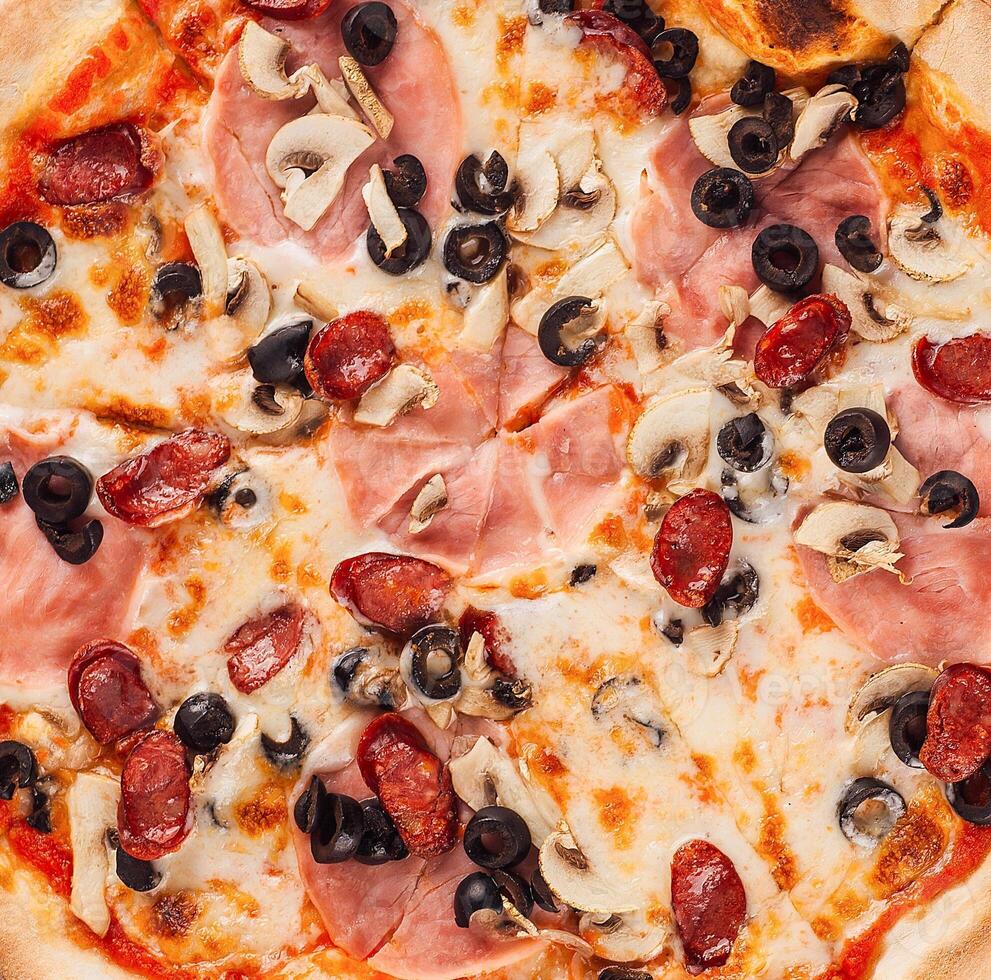 Delicious pizza closeup with melted cheese, salami, mushrooms and black olives photo
