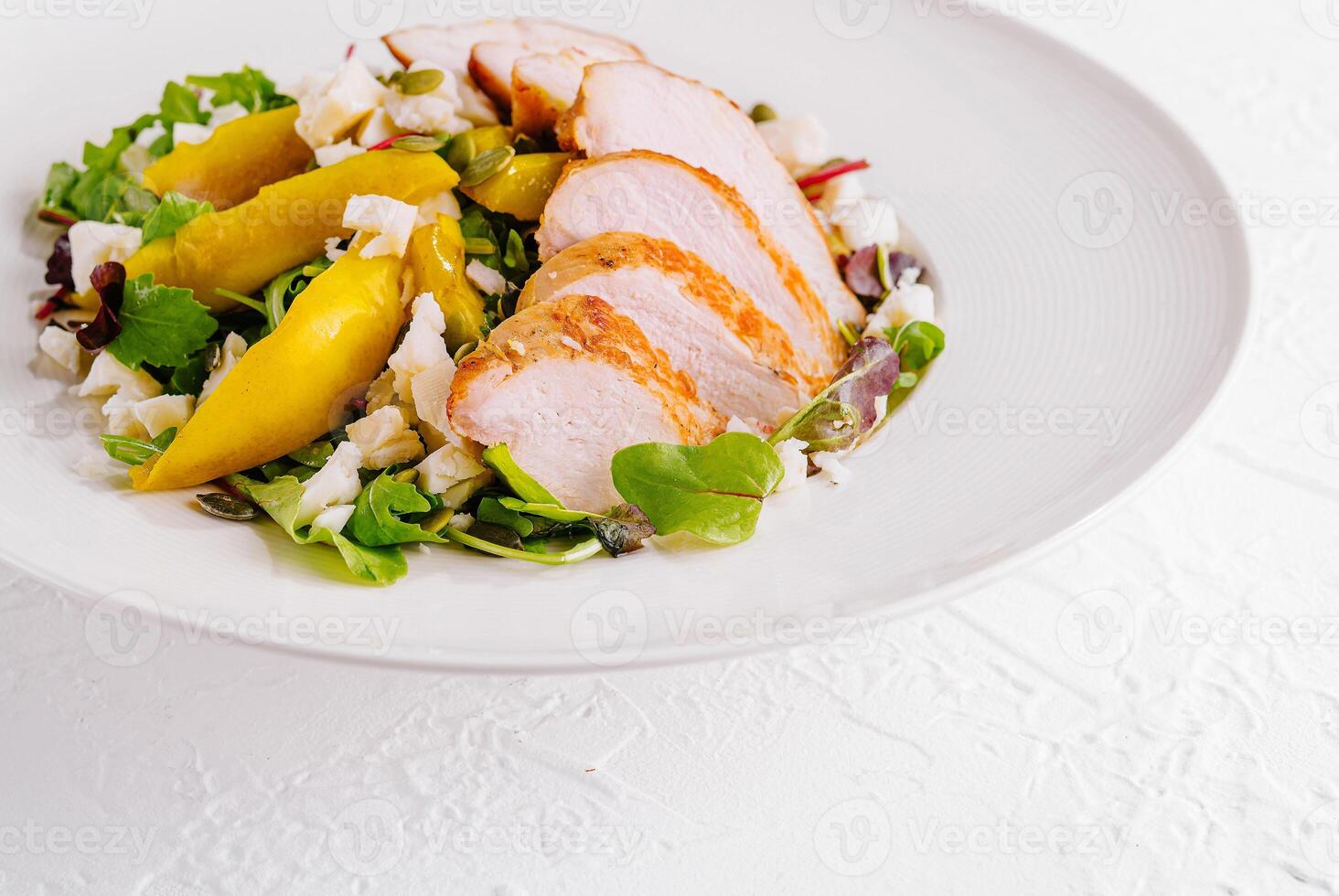 Grilled chicken breast salad with yellow bell peppers and feta cheese on white plate photo