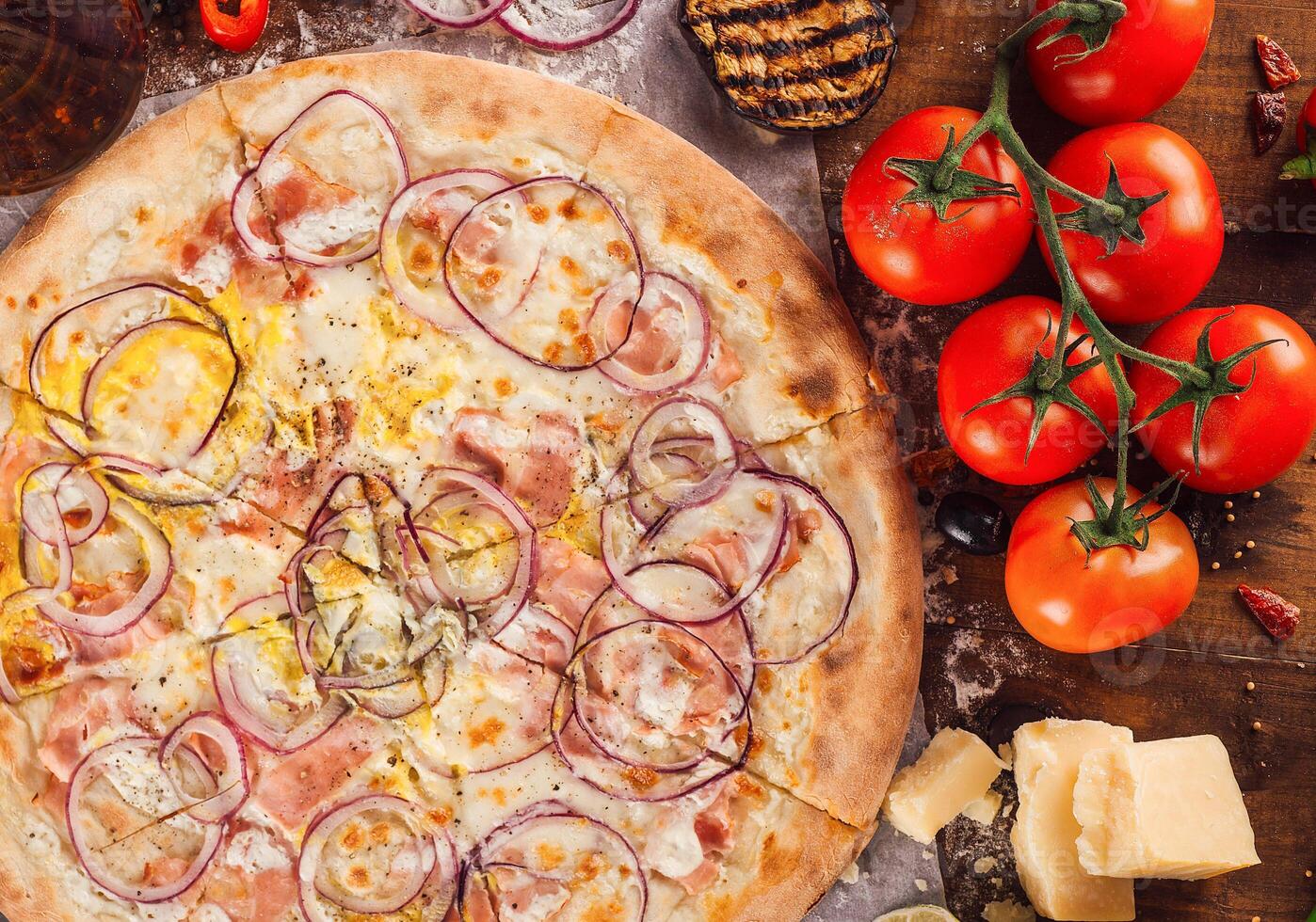 Delicious pizza with ham and onion rings lying on a wooden table photo