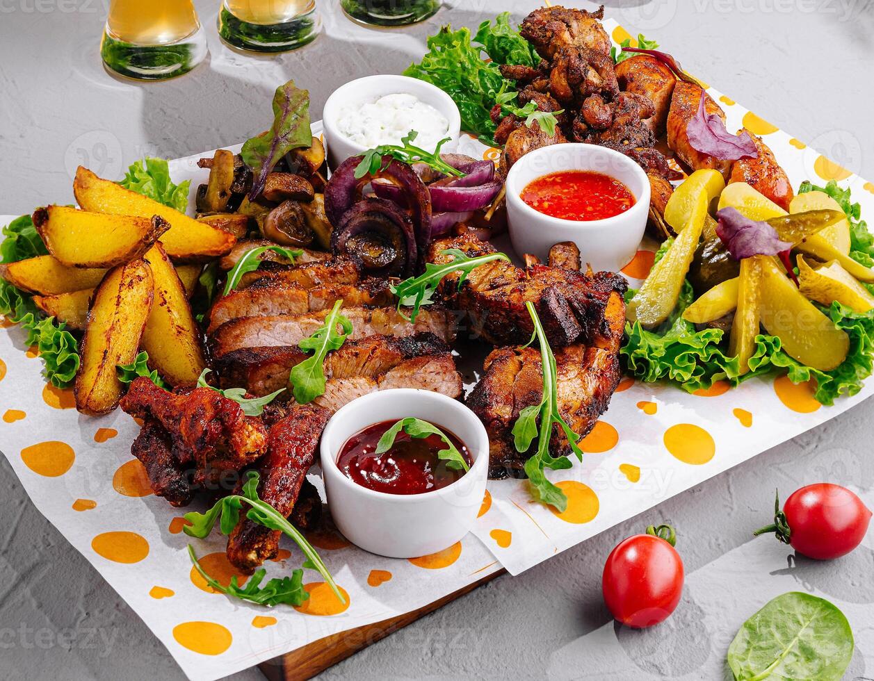 Delicious grilled meat assortment with sauces and potatoes being served on table photo