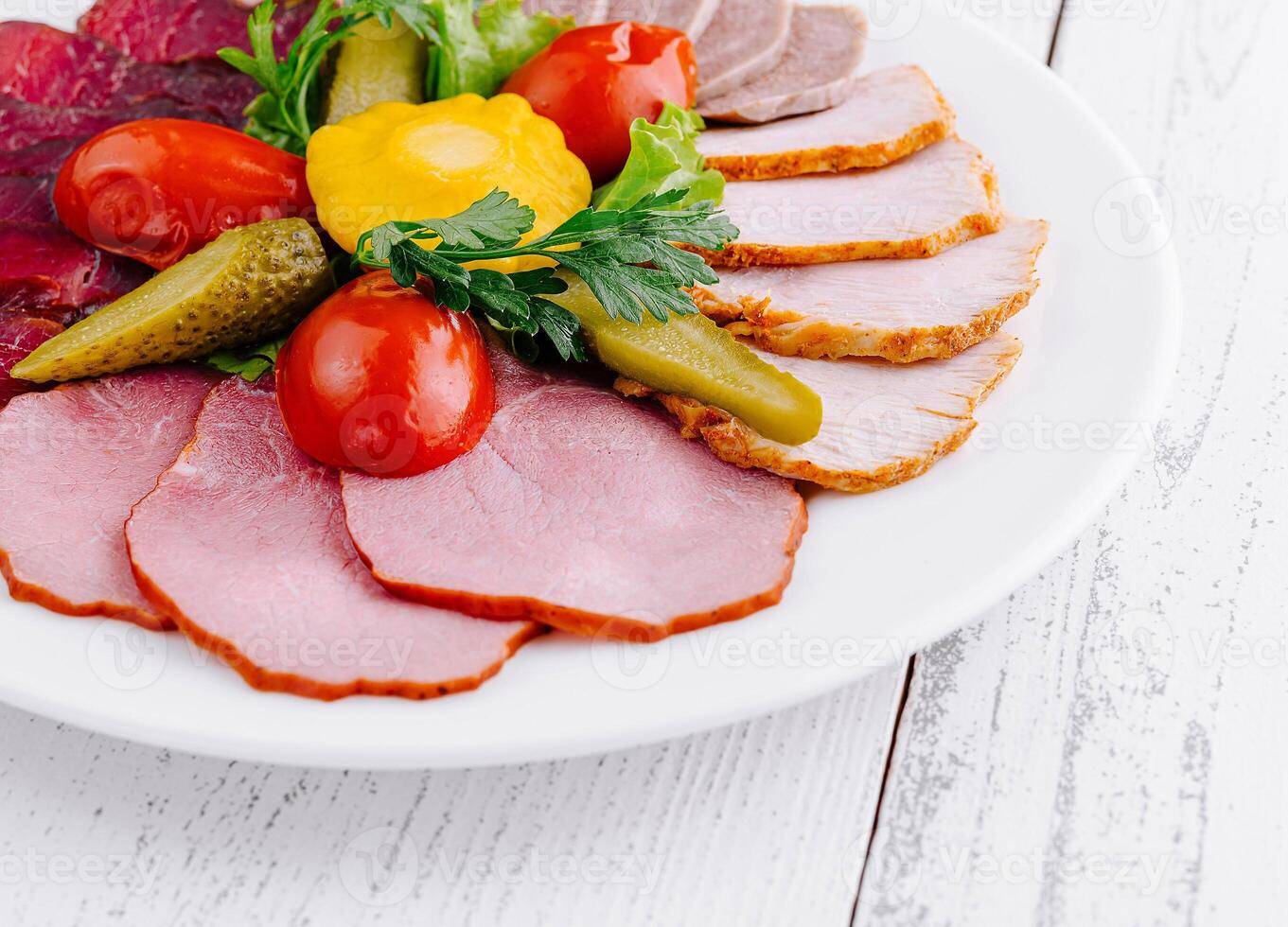Plate combining several types of meat cuts and pickles being served on white table photo