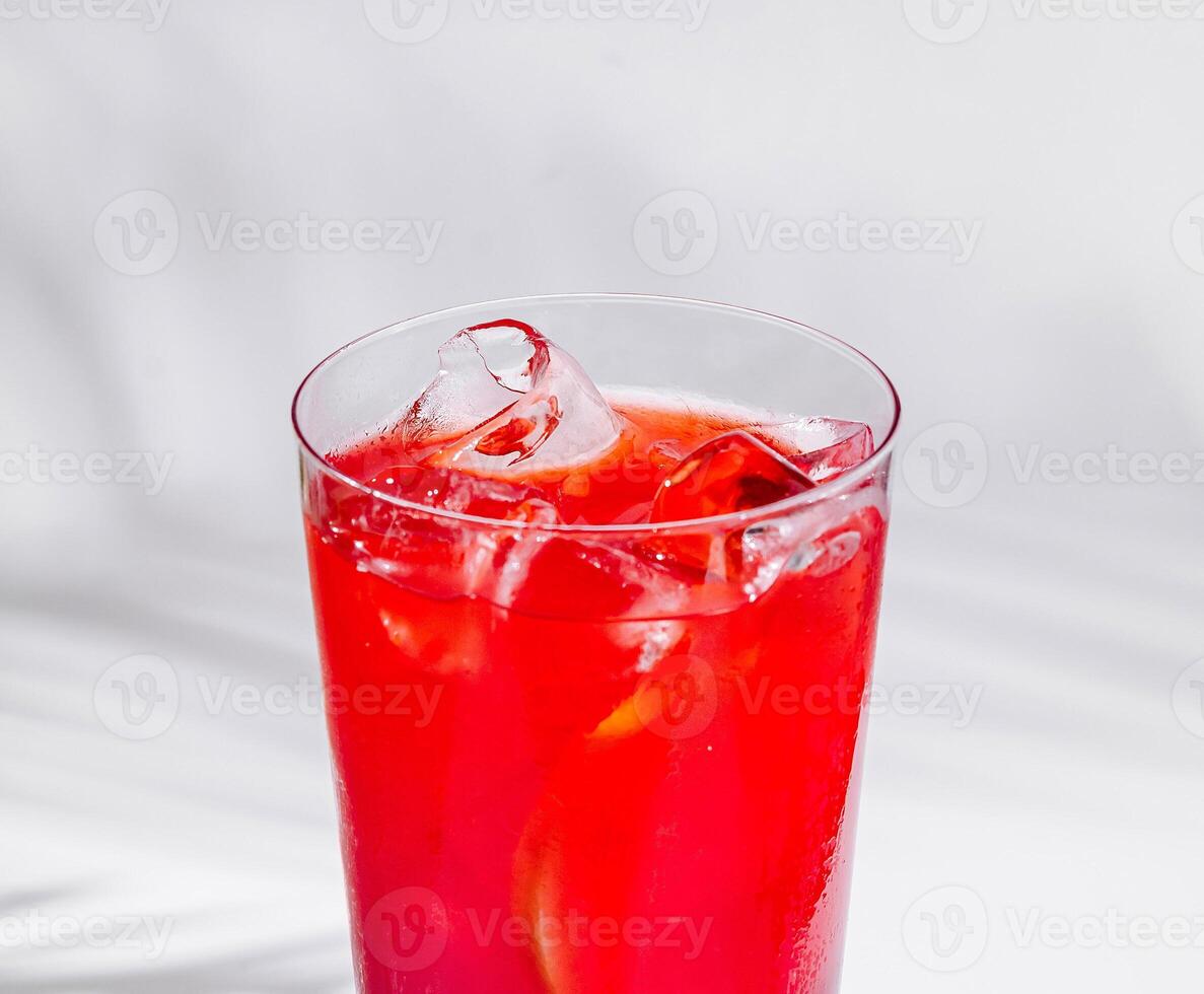 Refreshing red cocktail standing on white cube with tropical palm leaf shadow photo