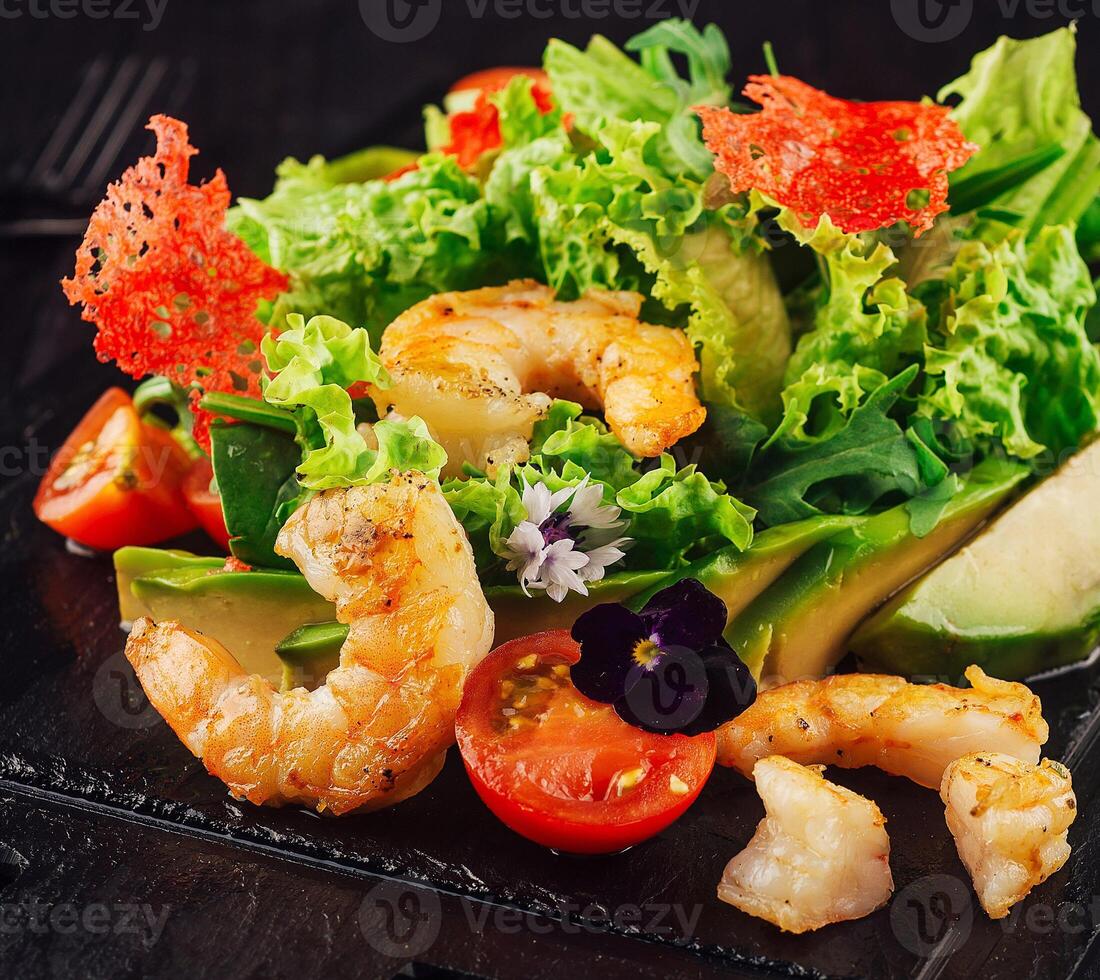 Delicious salad with grilled shrimps and avocado on dark stone background photo