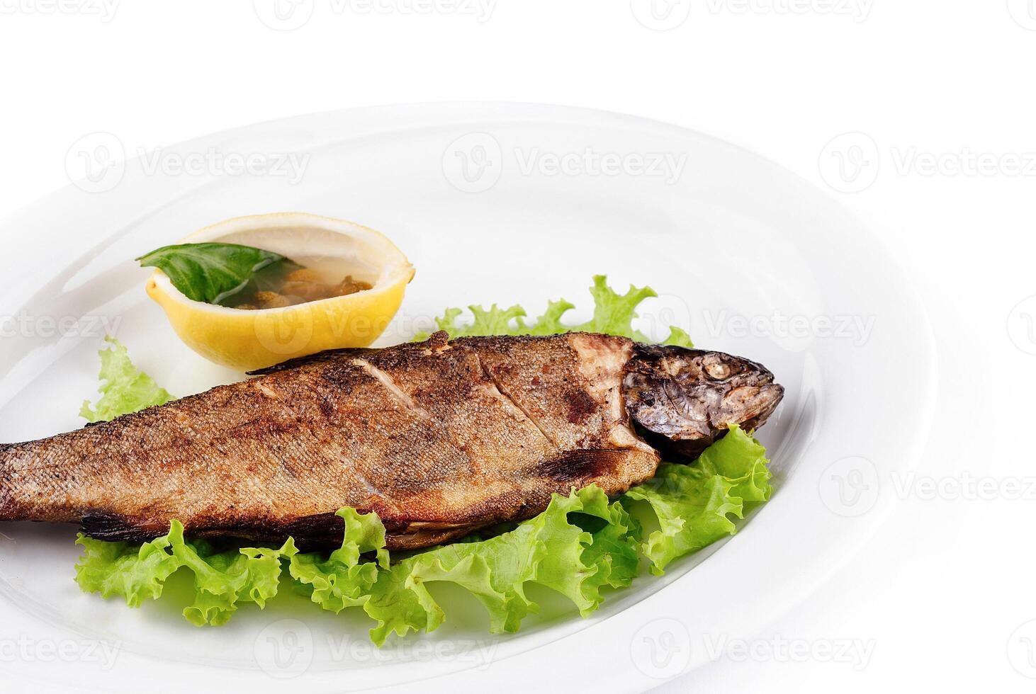 Grilled trout served on bed of lettuce with lemon and condiment photo