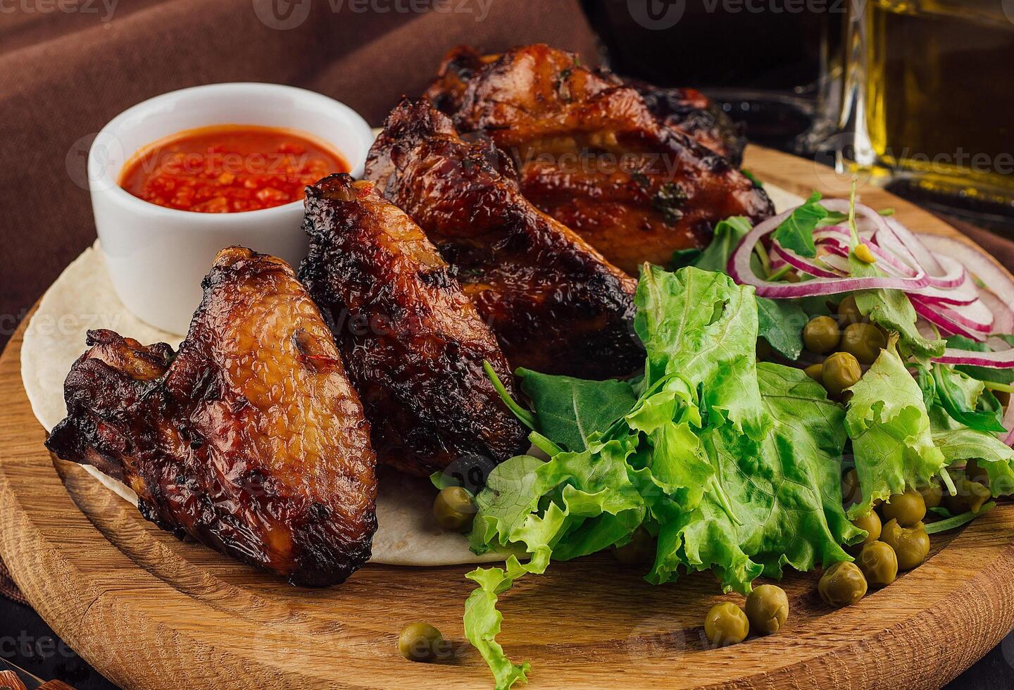 Grilled chicken wings served on wooden board with salad and sauce photo